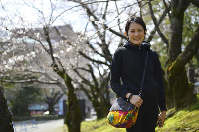 Portrait of smiling young woman with shoulder bag standing at park