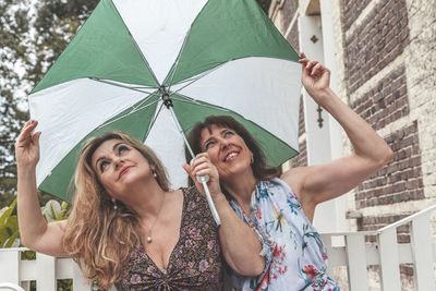 Couple of two attractive fifty year old women with umbrella in front of french villa on a rainy day