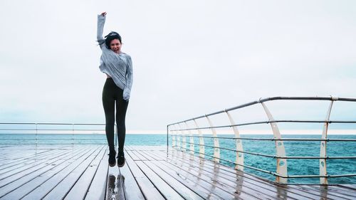 Cheerful woman jumping on pier against sky