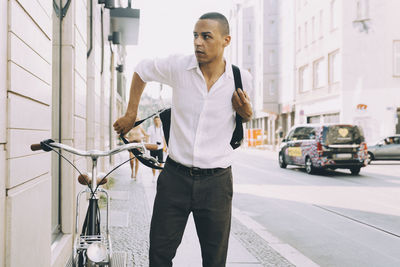 Businessman with bicycle standing on sidewalk against building in city