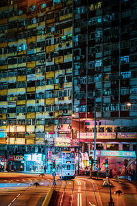 Illuminated street by buildings in city at night