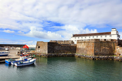 High angle view of boats moored on river by buildings against cloudy sky