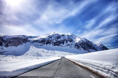 Road leading towards snowcapped mountain against cloudy sky