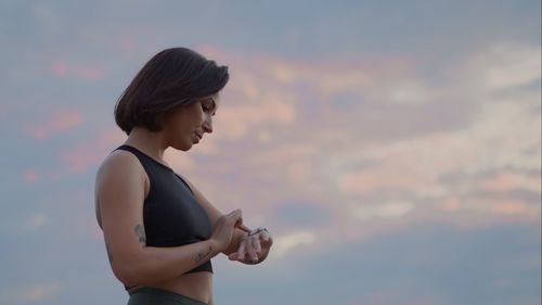 Side view of young woman standing against sky