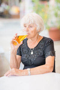 Mature woman sitting at a table in a summer cafe and drinking beer