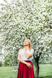 Mid adult woman with eyes closed standing against cherry blossom
