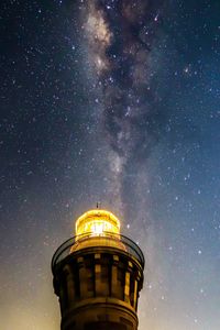 Low angle view of illuminated lighthouse against star field at night
