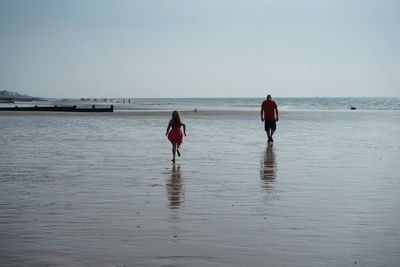 Rear view of men walking on beach against clear sky