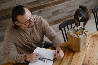 Man is working, writing with wild bird at home by the table. making noted, memories, diary with