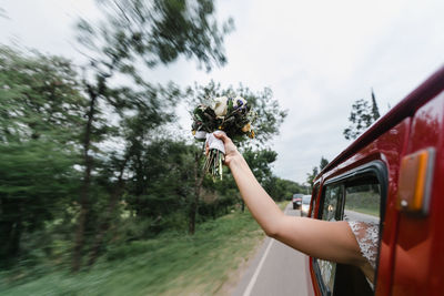 Cropped hand of bride holding bouquet through car window