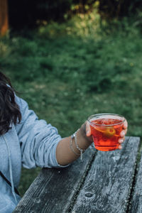 Woman holding aperol spritz aperitif cocktail outdoors at picnic table