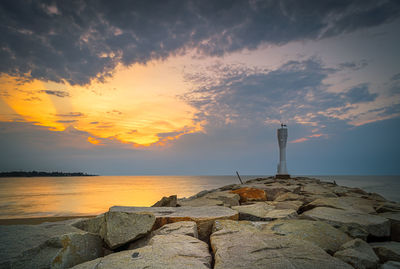 Lighthouse by sea against sky during sunset