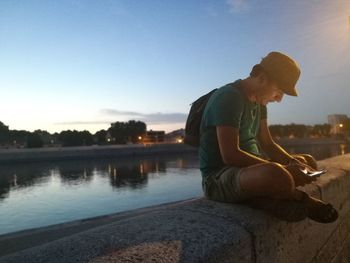 Side view of man sitting on rock against sky during sunset