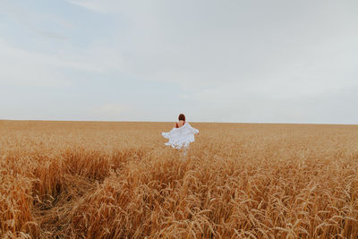 Rear view of woman running on field against sky