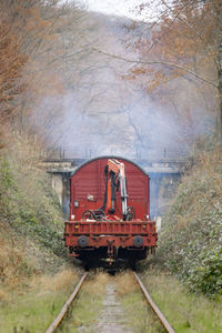 Rear view on maintenance train wagon with crane driving on single train track through autumn forest.