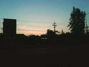 Silhouette of trees and house against sky at sunset