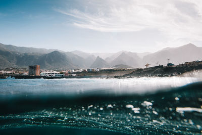 Scenic view of sea by mountain against sky