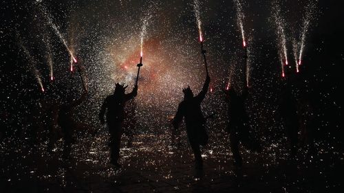 Silhouette people with firework display at night