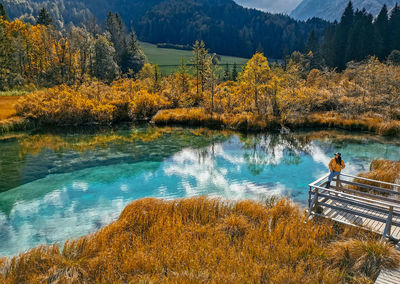 Woman sitting on wooden deck by turquoise lake surrounded by idyllic nature in autumn.