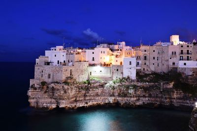 Scenic view of rocky coastline and city of polignano, italy at night