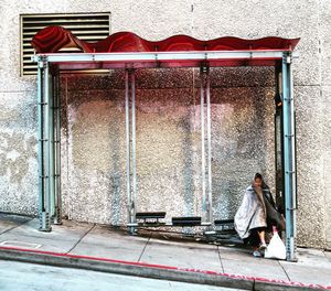 Full length of homeless person sitting at bus stop