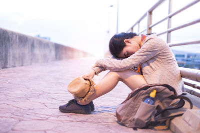 Young woman looking down while sitting on footpath