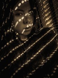 Close-up portrait of young woman by blinds