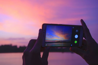 Close-up of hand holding mobile phone against sunset sky