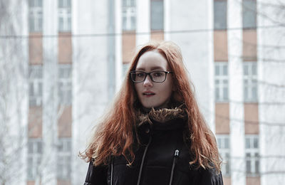 Portrait of beautiful young woman standing against building in city