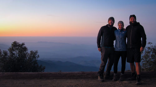 Portrait of friends standing against landscape and sky during sunset