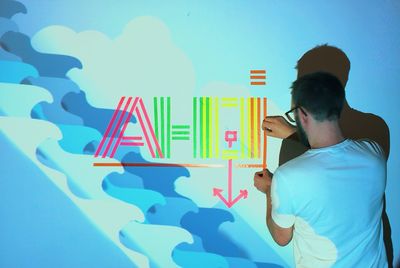 Rear view of man creating text from multi colored papers on wall at home with projection light