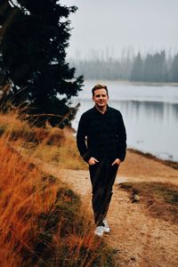 Young man standing at lake against foggy sky 