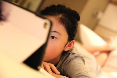 Girl looking at digital tablet while lying on bed at home