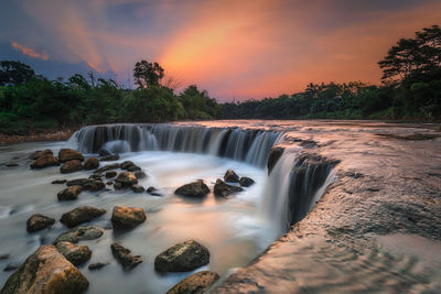 Scenic view of waterfall against sky during sunset