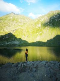 Rear view of man standing on rock by lake against sky