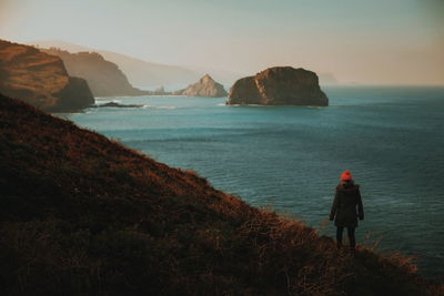 Rear view of woman standing on rock by sea against sky