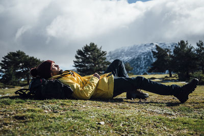 Young man with yellow jacket and backpack lying on the mountain.
