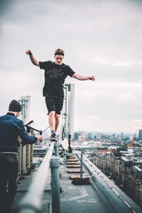 Man with arms raised in city against sky