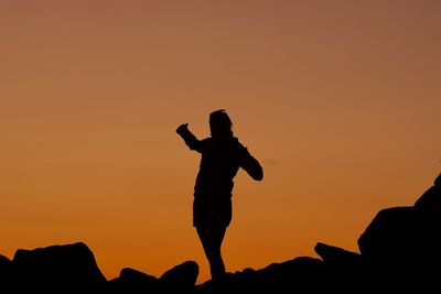 Silhouette woman standing on rock against orange sky