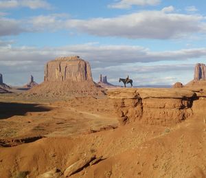 Woman riding horse on rocks against sky