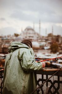 Rear view of man standing on railing against sky