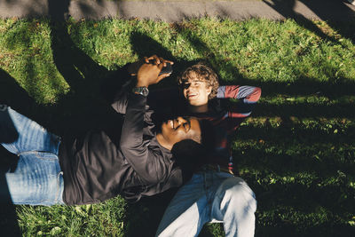 High angle view of smiling male friends taking selfie while lying on grass in park