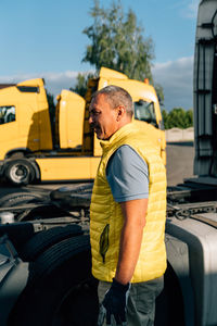 Side view of young man standing against car