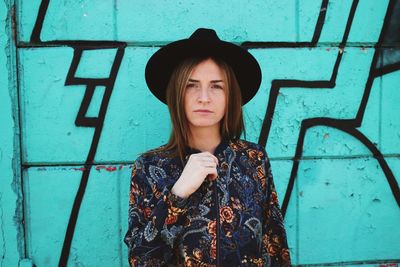 Portrait of woman in hat standing against graffiti wall