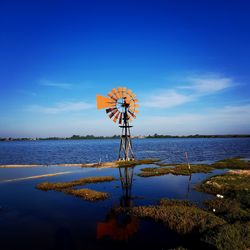 Traditional windmill at lake against blue sky