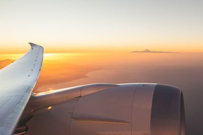 Cropped image of airplane wing against sky during sunset