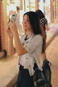 Young woman photographing with mobile phone in city at night