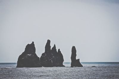 Rock formations by sea against clear sky