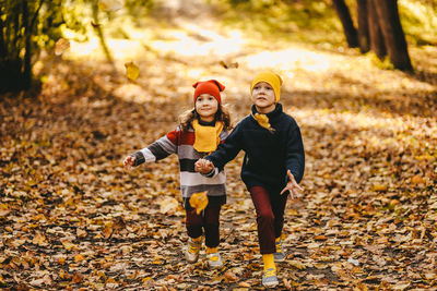 Happy cheerful children in warm clothes have fun walking running in autumn park playing with leaves