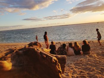 People at beach against sky during sunset